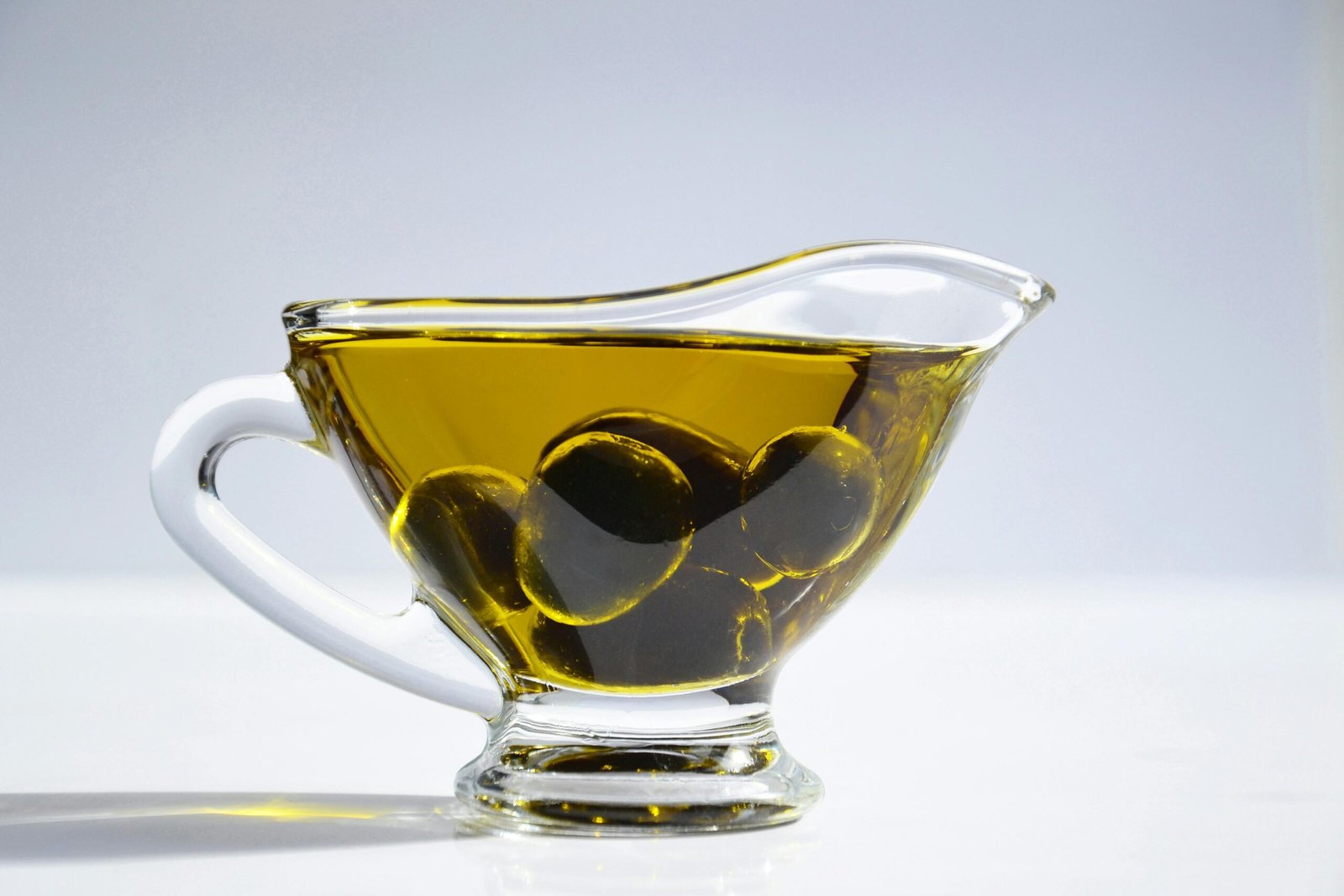 Menu High-resolution image of a glass cup filled with olive oil and olives, ideal for culinary themes.