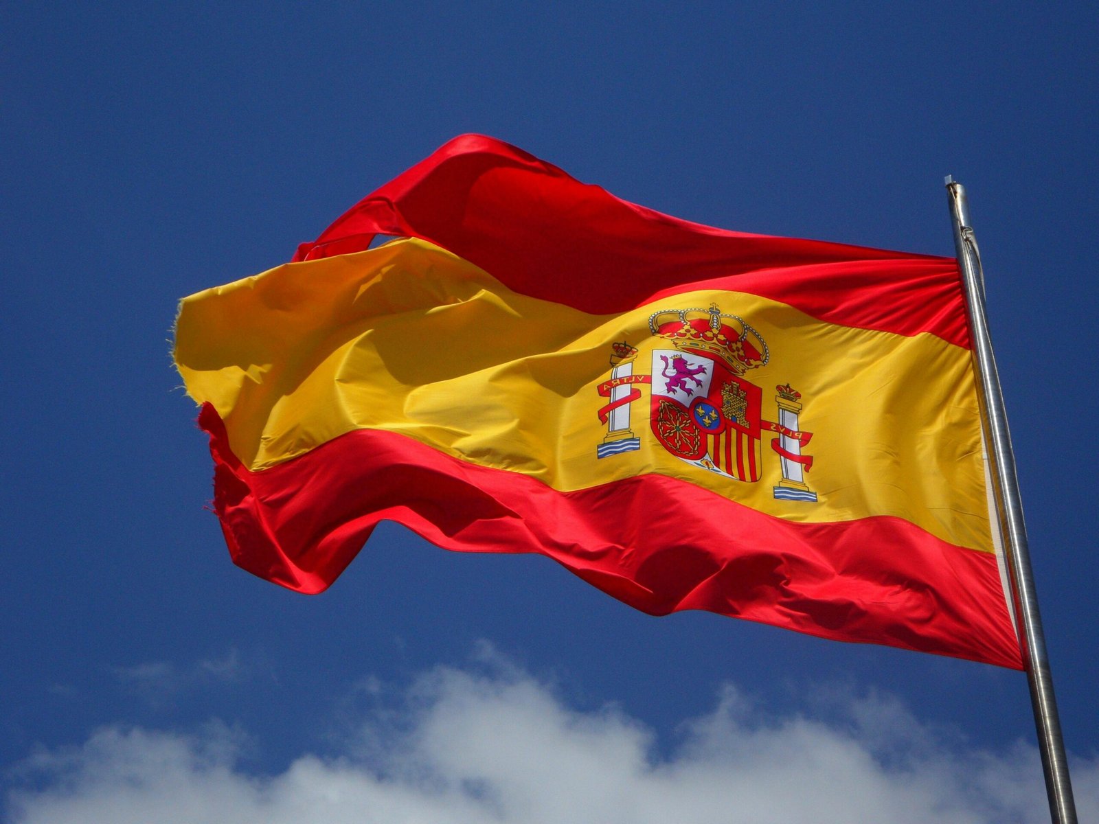 Menu Vibrant Spanish flag waving against a clear blue sky and clouds.